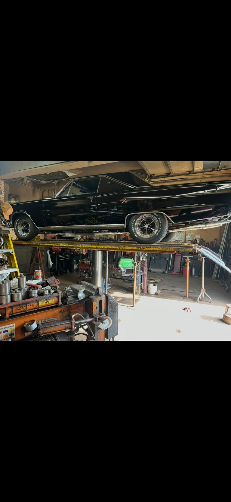 Black classic car lifted on hydraulic platform in garage with toolbox and equipment visible below