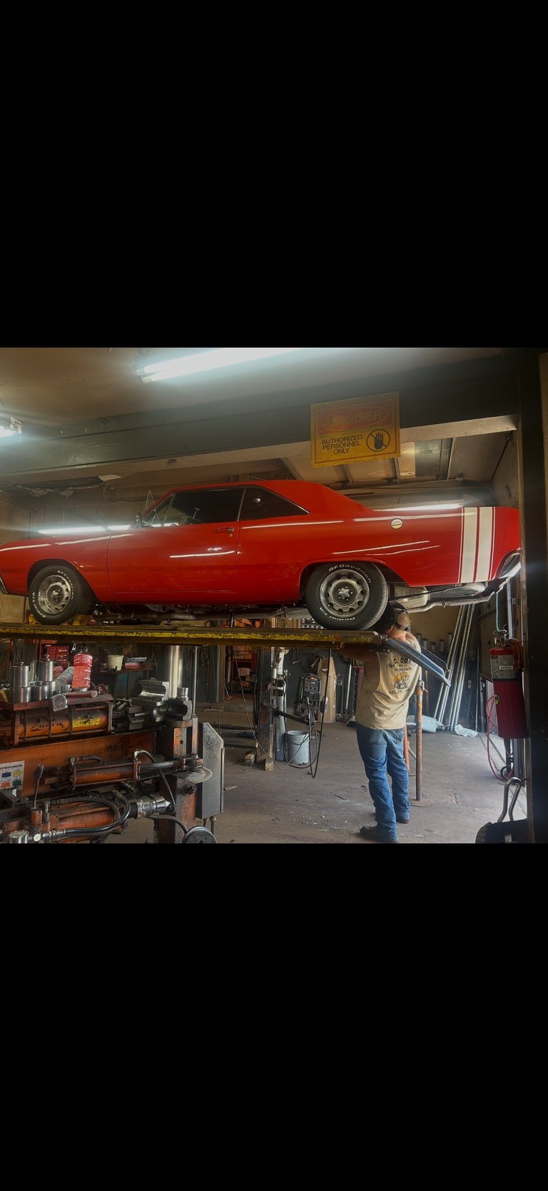 Red vintage car elevated on a garage lift with a mechanic working underneath in an automotive workshop