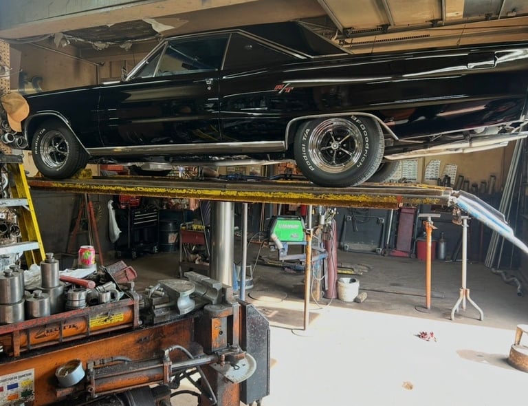 Black vintage car elevated on garage lift with workbench and tools below